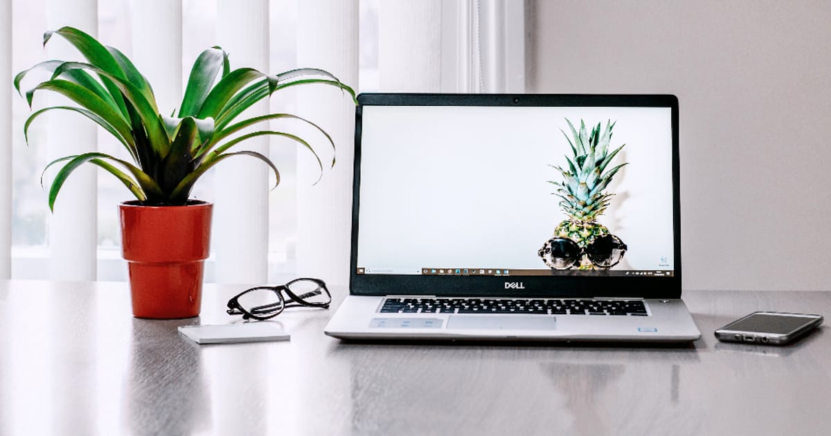 A laptop open on a desk beside reading glasses and a notebook
